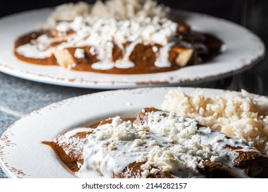 Typical Mexican Food. Mole Enchiladas. Fried Tortillas With Chicken Inside And Mole Sauce On Top. 2 White Plates On A Black Background