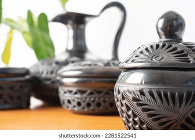 Typical Mexican handicraft. Set of black clay pots handmade in Oaxaca, Mexico. White background, wooden base and a plant in the background. - Shutterstock ID 2281522541