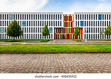 Typical Modern New Office Or College School Building Exterior. Backyard With Parking Lots, Lawn, Trees And Road