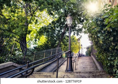 Typical Montmartre Staircase In Paris, France With Old Street Lamp And Sunlight Coming Through The Trees