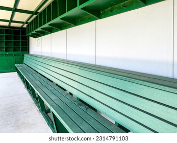 typical nondescript high school baseball, softball dugout with green bench and gray walls. No people visible. Not a ticketed event.	