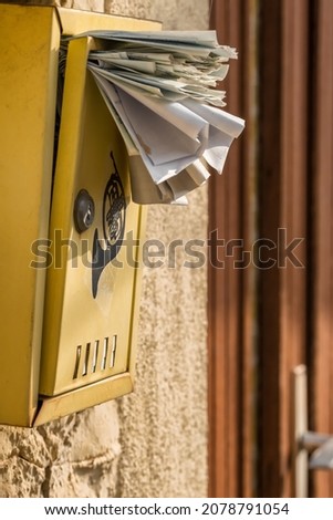 Typical overfull old post box. Yellow mail box on a wall full of letters and spam flyers