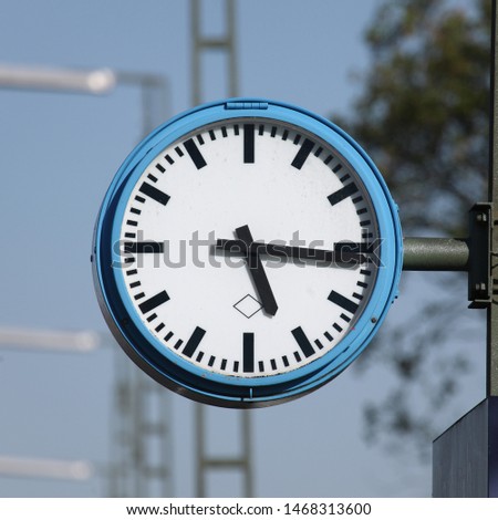 Typical platform clock in German train stations. Black fingers and numbers on white clock face. Blue case. Time on clock: 05h16