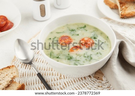 Typical Portuguese soup Caldo Verde with bread and chorizo sausage on gray background