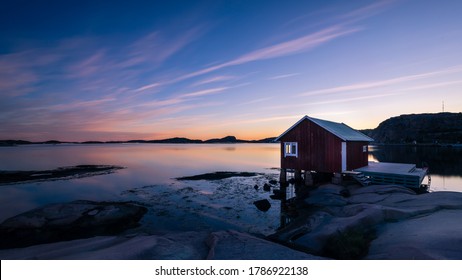 A Typical Red Boat House With A Colorful Sky With Reflections In The Ocean On The Swedish West Coast, Bohuslän