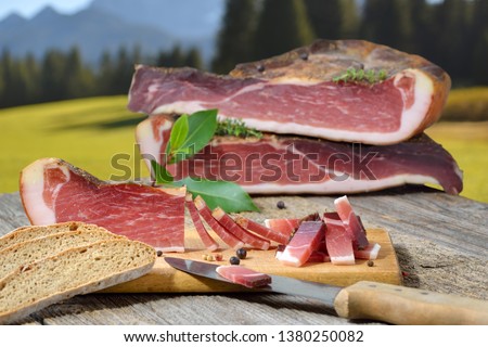 Typical South Tyrolean bacon snack with local rye bread lying on a rustic table in front alpine pastures and mountains of the alps
