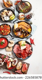 Typical spanish tapas concept. Concept include jamon, chorizo sausage, brushettas, bowl with olives, shrimp, pan with paella, cheese, sangria, churros on a white background. Top view.