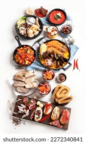 Typical spanish tapas concept. Concept include jamon, chorizo sausage, brushettas, bowl with olives, shrimp, pan with paella, cheese, sangria, churros on a white background. Top view.