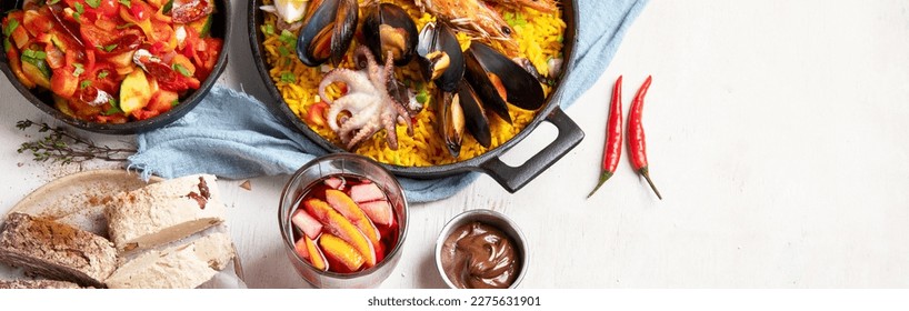 Typical spanish tapas concept. Concept include jamon, chorizo sausage, brushettas,  olives, shrimp, pan with paella, cheese, sangria, churros on a white background. Top view. Panorama with copy space.