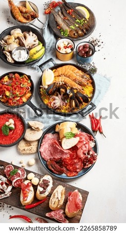 Typical spanish tapas concept. Concept include jamon, chorizo sausage, brushettas, bowl with olives, shrimp, pan with paella, cheese, sangria, churros on a white background. Top view.