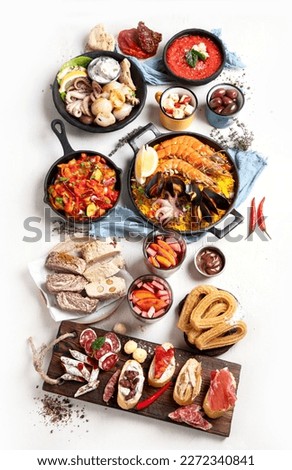 Typical spanish tapas concept. Concept include jamon, chorizo sausage, brushettas, bowl with olives, shrimp, pan with paella, cheese, sangria, churros on a white background. Top view.