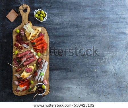 Typical spanish tapas concept. include variety slices jamon, chorizo, salami, bowls with olives, peppers, anchovies, spicy potatoes, mashed chickpeas on a wooden table. Copyspace