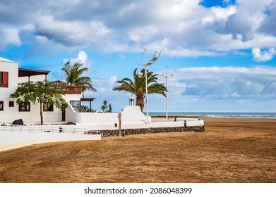 Typical white houses on beach of Playa Honda on Lanzarote island, Spain. Vacation home near sea with palm trees and sandy beach under blue sky on Canary Islands