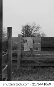 Typical Wooden Fence Down On The Farm With Dirty Towels And Laundry Air Drying From The Railing In Black And White.