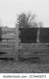 Typical Wooden Fence Down On The Farm With Dirty Towels And Laundry Air Drying From The Railing In Black And White.