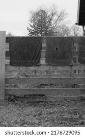 Typical Wooden Fence Down On The Farm With Dirty Towels And Laundry Air Drying From The Railing In Black And White.