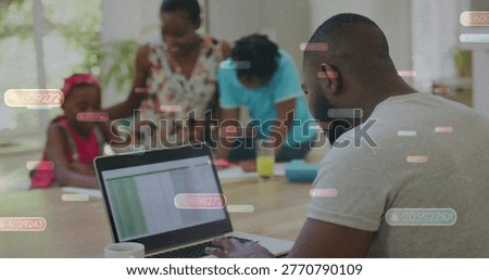 Typing man in gray T-shirt working on laptop at kitchen table, with spreadsheet overlay, copy space. Family, homeoffice, workfromhome, collaboration, sunlit, diningroom, computer