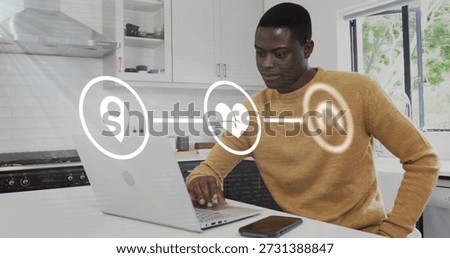 Typing man in mustard sweater using laptop at kitchen island, phone and digital icons, copy space. Workfromhome, person, countertop, computer, smartphone, modern, minimalist