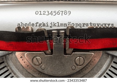 typing with an old typewriter. The numbers from 0 to 9 and the lowercase alphabet, written on a white sheet of paper, with a two-tone, black and red ribbon, and the rest of the steel mechanisms