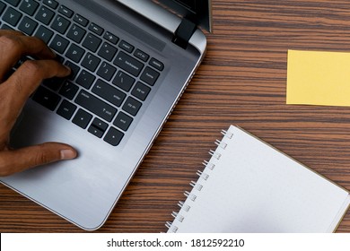 Typing on a keyboard while working on a project. A lap top, a mobile, calculator and plant are also on display on this brown striped working table.