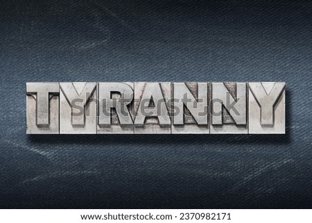 tyranny word made from metallic letterpress on dark jeans background