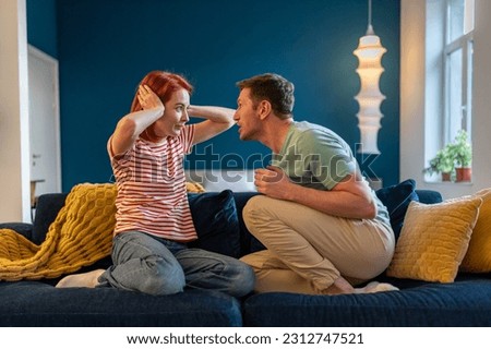 Tyrant husband shouting on wife sitting on couch at home looking at her face. Scared woman closing ears. Domestic violence, abuse, neurotic relationships, toxic couple relations, marital discord.