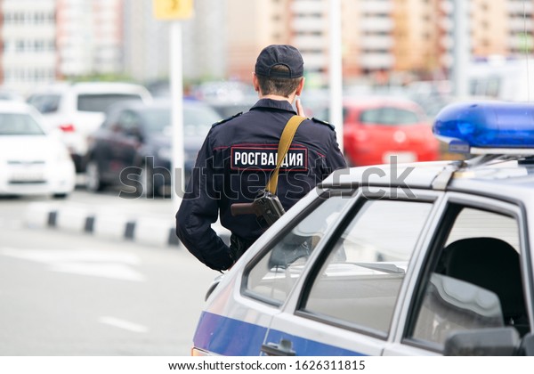 Tyumen region / Russia -\
7/06/2019:Russian police. A policeman with a gun stands near a\
company car.