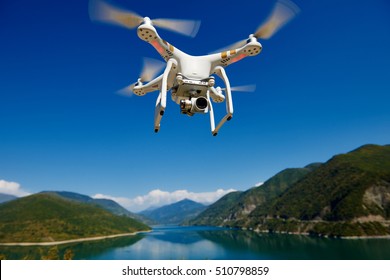 Uav Drone With High Resolution Digital Camera Flying In The Blue Sky Over The Mountain At Lake