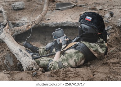 UAV operator with a remote control sitting in a trench. The concept of unmanned technologies in modern warfare. bombing reconnaissance drone. A soldier controls a drone. the remote control is in hands