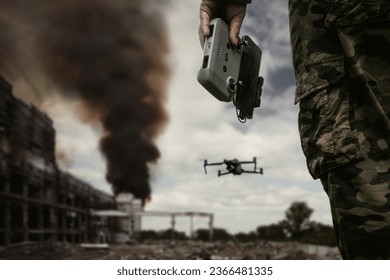 UAV operator with a remote control stands against the background of a destroyed building with black smoke in city. The concept of unmanned technologies in modern warfare. bombing reconnaissance drone