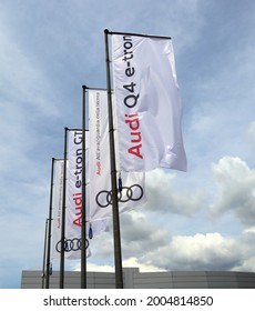 Udine, Italy. Juy 3, 2021. Promotional Flags For The Electric Car Model Q4 GT E-tron Outside The Audi Car Dealership Of The Area, Against A Blue Sky With Clouds.