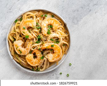 Udon noodles with fried shrimps, squid rings, red onion and napa cabbage decorated with chopped green onion and sesame seeds. Traditional asian cuisine. Concrete background, top view, copy space.
