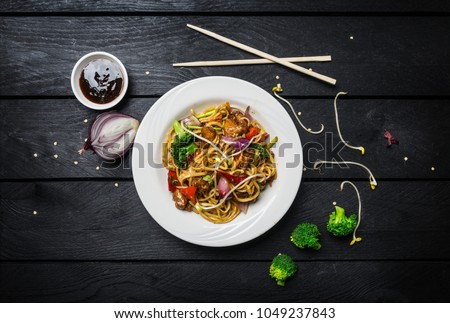 Udon stir fry noodles with meat or chicken and vegetables in a white plate with chopsticks.