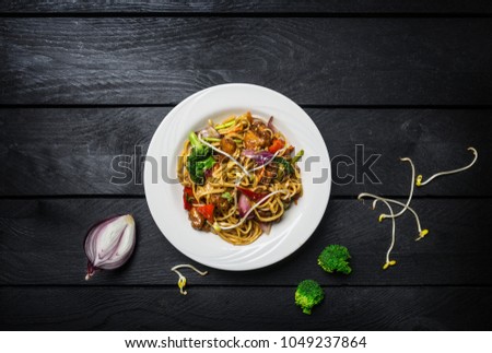 Udon stir fry noodles with meat or chicken and vegetables in a white plate.