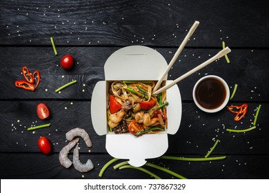 Udon stir fry noodles with seafood in a box on black background. With chopsticks and sauce.