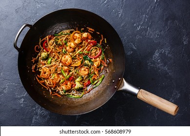 Udon stir-fry noodles with shrimp in wok pan on dark stone background