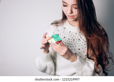 UFA, RUSSIA - JANUARY 14, 2018: An Attractive Brunette Woman With Long Hair Solves A Puzzle, A Two-sided Rubik's Cube On A White Background. Focus On The Cube