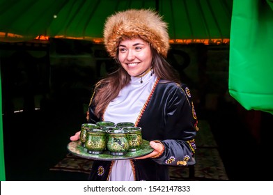 UFA, RUSSIA. July 12, 2019. A Girl In A Traditional Bashkir Dress With A Fox Fur Hat Meeting Guests With A Tray With Glasses Filled With Kumis (kumys), A Fermented Horse Milk, A Refreshing Drink.