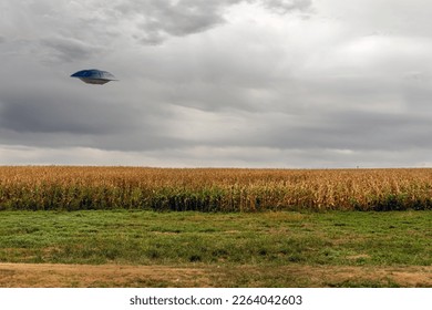 UFO flying Saucer flying over a cornfield against a cloudy sky.