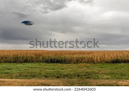 UFO flying Saucer flying over a cornfield against a cloudy sky.