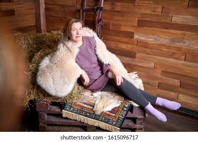 Ugly Adult Aged Woman In A Fur Cape On The Couch With Hay In The Room Or In The Hayloft With Wooden Walls. Rustic Style In The Interior During Photoshoot