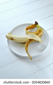 An Ugly Banana Begins To Deteriorate. It Lies On A Round White Plate.