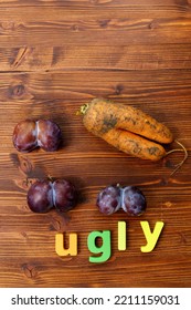 Ugly Organic Blue Plums And Carrot On Wooden Background. The Ugly Produce Trend Is The Sale Of Imperfect Looking Produce. Vertical Photo