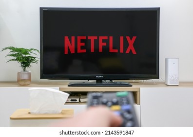 UK - April 5th 2022: Watching Netflix (logo) On Television Screen, Hand Holding Remote Control In Foreground Out Of Focus, First Person Perspective, Depicting Home Life, Selective Focus