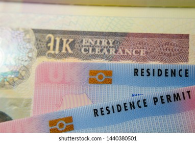 UK BRP (Biometrical Residence Permit) Cards For Tier 2 Work Visa Placed On Top Of UK Entry Clearance Vignette Sticker In The Passport. Close Up Photo. 