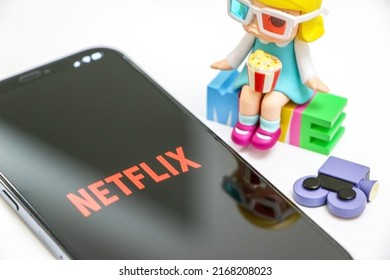 UK - June 6th 2022: Netflix on smartphone, Netflix logo on display screen, by movie-themed toy doll and sign, online streaming and movie concept