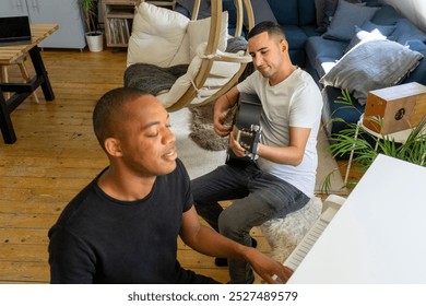 UK, London, Gay couple playing piano and guitar at home - Powered by Shutterstock