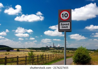 UK road sign 10 mph speed limit. The country road leads to a power station. Blue cloudy sky.