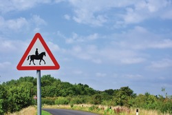 UK Road Sign Accompanied Horses Or Ponies Likely To Be In Or Crossing Road Ahead Against A Blue Cloudy Sky.