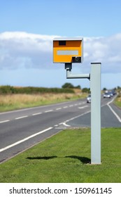 UK Static Speed Camera With Speeding Cars Approaching On A Rural Road